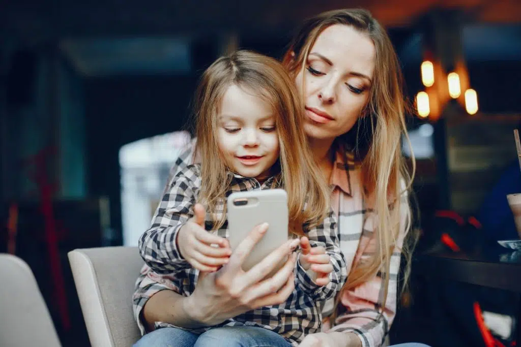 une femme assise au restaurant a sa fille sur les genoux. elle tient son téléphone portable devant sa fille qui le regarde en souriant.