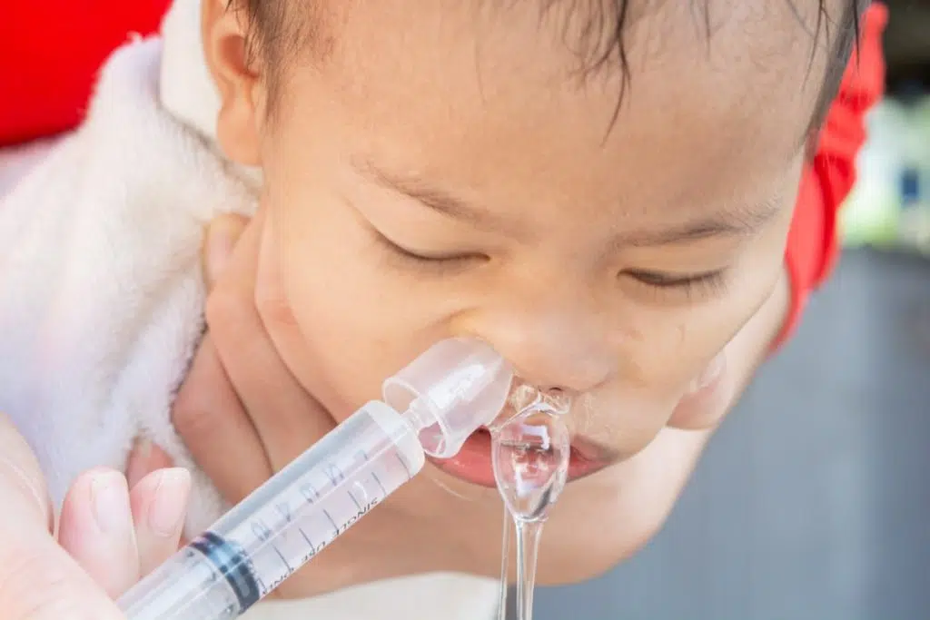 un bébé reçoit du sérum physiologique dans le nez et son nez coule fortement afin d'évacuer le mucus