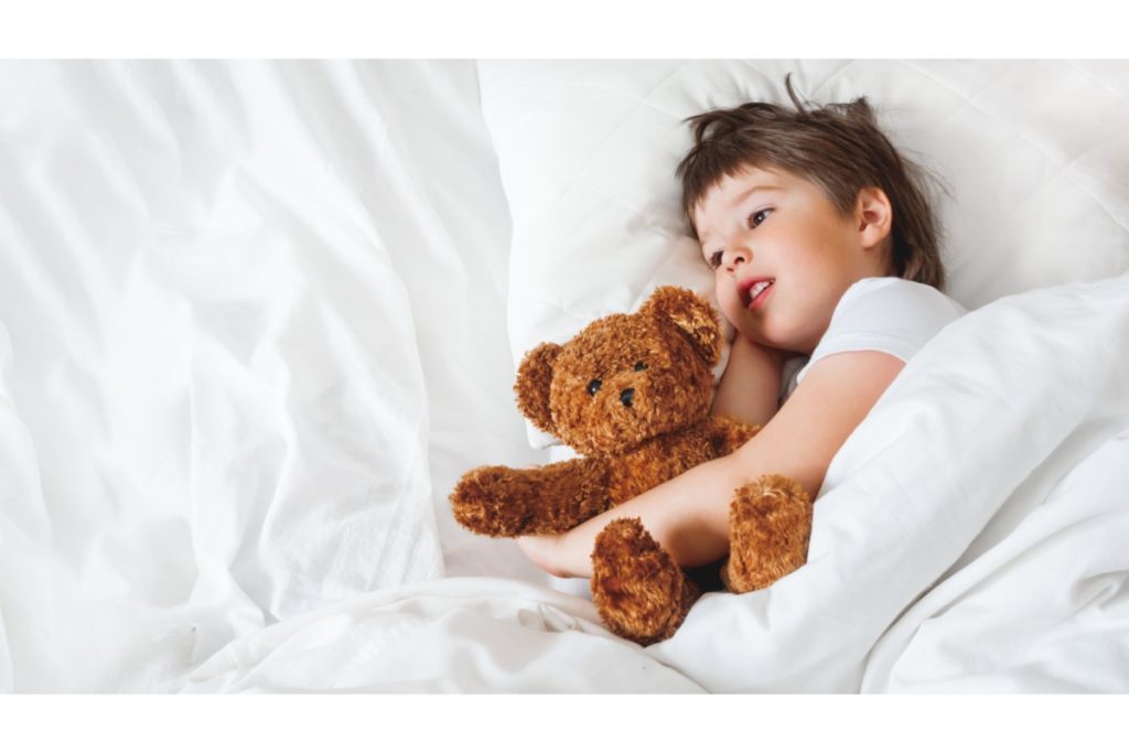 Tout-petit est au lit avec un joli ours en peluche. Petit garçon sous couverture blanche avec peluche. La protection en peluche surveille le sommeil de l'enfant.