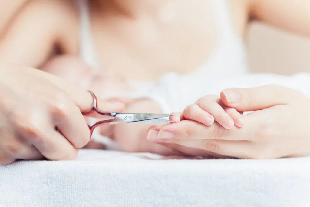 vue rapprochée de mains d'adulte tenant une main de bébé pour lui couper les ongles avec un ciseau