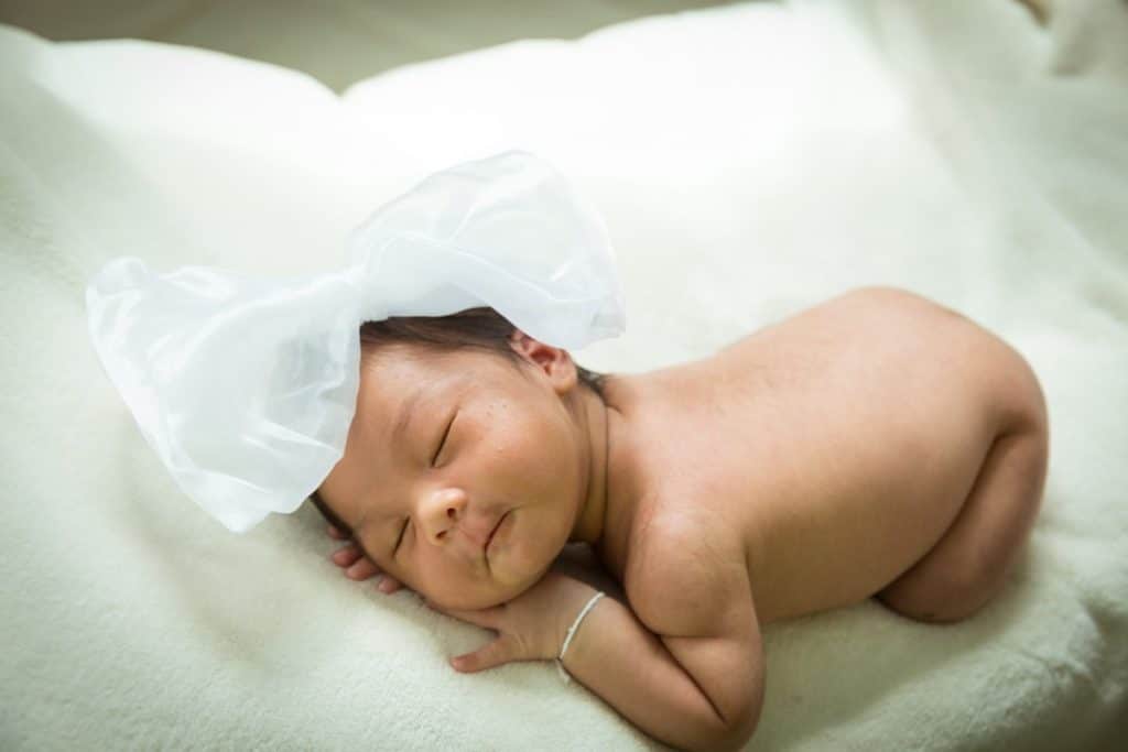 un bébé dort nu sur une couverture blanche avec un noeud blanc géant sur sa tête.