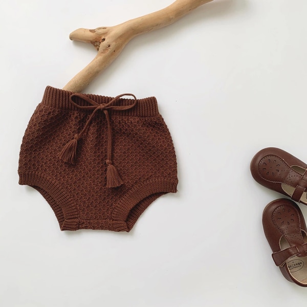 Short tricoté en coton pour bébé marron avec un fond blanc et des petites chaussures pour bébé sur le côté