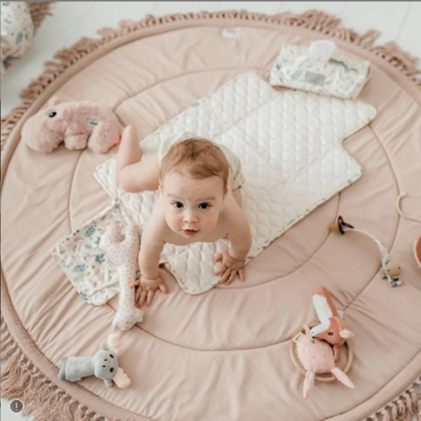 Tapis de sol rose pour bébé avec un bébé en couche qui apparait dessus ainsi que des jouets éparpillés