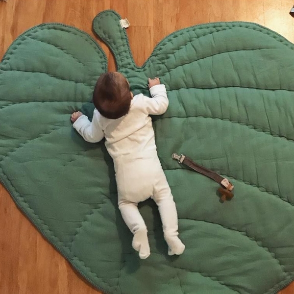 Tapis de parc pour bébé en forme de grande feuille verte avec un bébé installé dessus