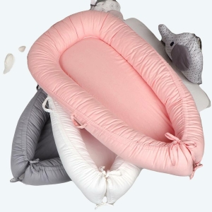 3 Réducteurs de lit , un rose, une blanc et un gris, empilé dans un lit à barreaux pour enfants