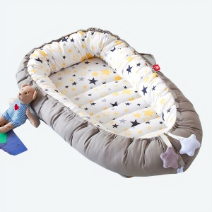 Couffin réducteur de lit avec le tour marron et l'intérieur avec étoiles bleues et jaunes et un petit doudou ourson posé sur le bord