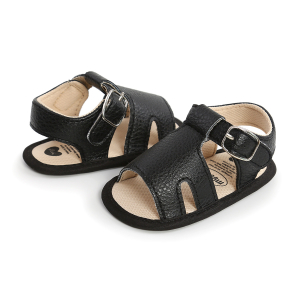 Sandale noire plate d'été pour bébé ouverte posée l'une à côté de l'autre dans deux sens opposés et posées sur un sol blanc