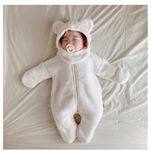 Bébé allongé et endormi sur un lit, qui porte une barboteuse moltonnée blanche