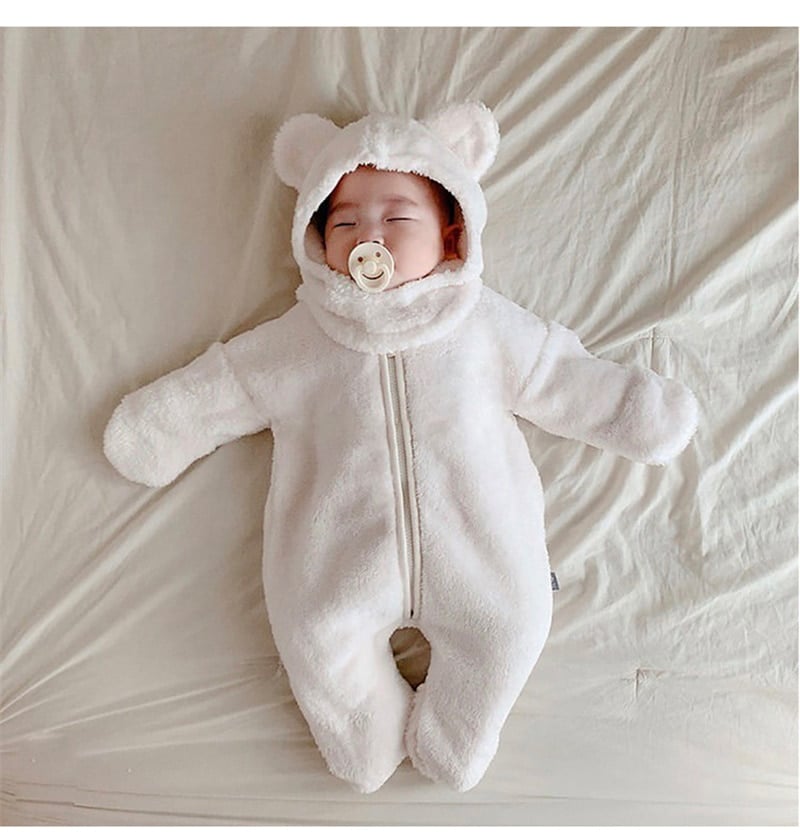Bébé allongé et endormi sur un lit, qui porte une barboteuse moltonnée blanche