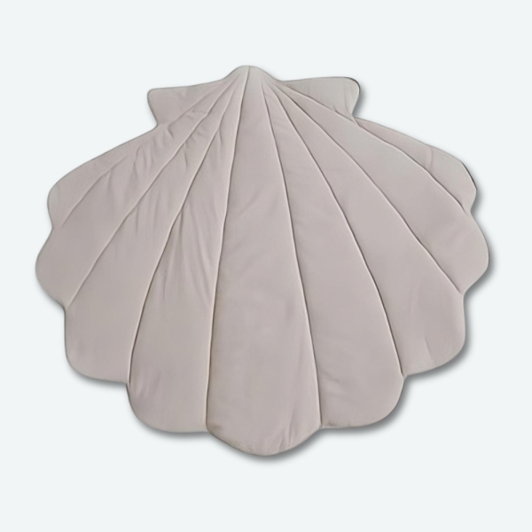 Un tapis de sol pour bébé de couleur beige en forme de coquillage. Celui-ci est en coton doux.