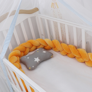 Lit de bébé blanc avec un voilage et un tour de lit tressé jaune avec un petit coussin gris avec étoiles blanches