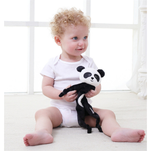 bébé blond et frisé, vêtu d'un body blanc, installé assis par terre, tient dans ses mains un doudou noir et blanc style chiffon avec une tête de panda mignon