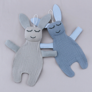 deux petits doudous du même modèle pour bébé en forme de poupée lapin en chiffon , ils ont les yeux fermés , l'un et bleu et l'autre gris, il sont posés l'un près de l'autre sur un sol gris