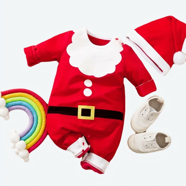 déguisement de papa noel pour bébé avec un petit chapeau de noel et un pyjama , près d'un arc en ciel, posé à plat au sol , sur la droite se trouve de petite chaussures