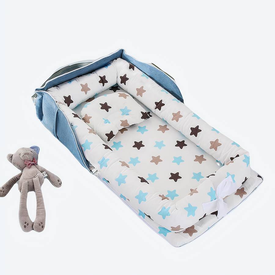 Réducteur de lit pour bébé bleu avec motifs étoiles, posé sur un lit avec des jouets et un doudou