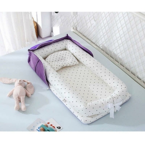 Réducteur de lit pour bébé violet à pois posé sur un lit avec des jouets et un doudou