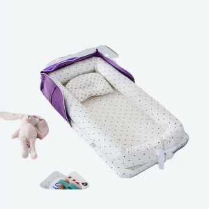 Réducteur de lit pour bébé violet à pois posé sur un lit avec des jouets et un doudou