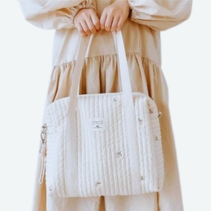 Poussette avec un sac à langer beige matelassé et brodé posé sur le guidon